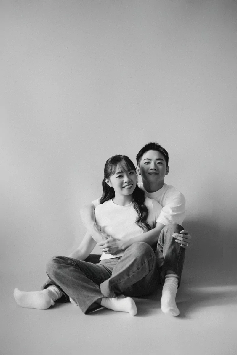 A black-and-white portrait of the couple sitting close together on a studio floor.