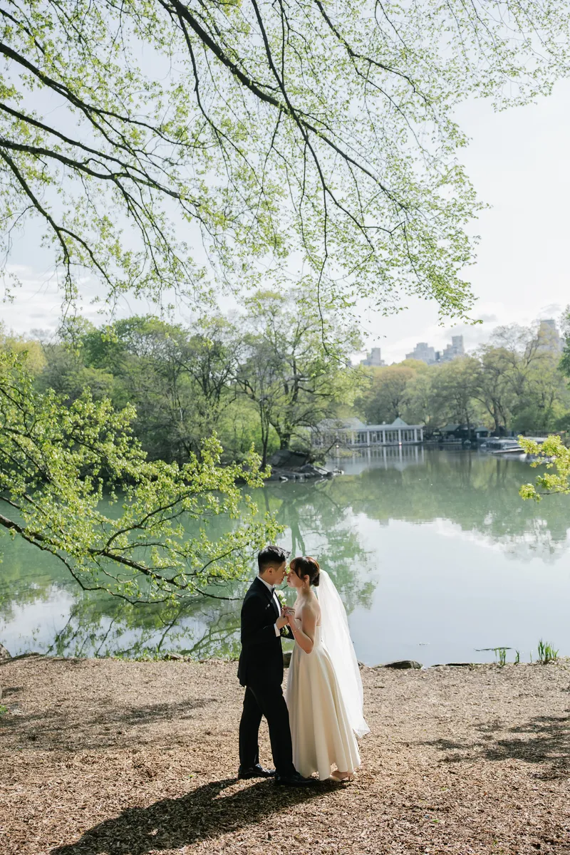 The couple sharing a quiet moment beneath green branches beside the lake.