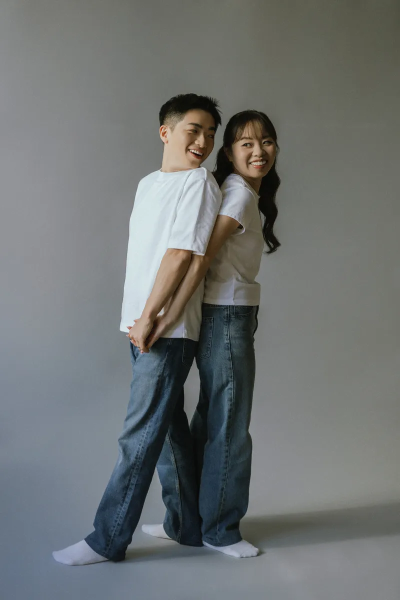 The couple smiling together in casual clothes against a simple studio backdrop.