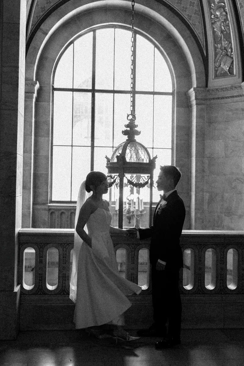 The couple holding hands in silhouette beneath an arched window and chandelier.